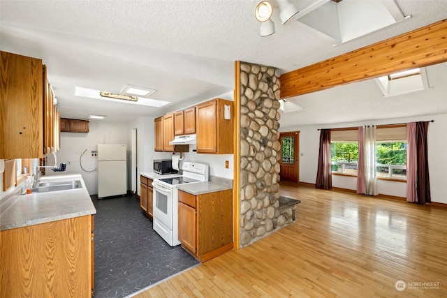 kitchen featuring white appliances, a textured ceiling, light hardwood / wood-style flooring, a skylight, and sink