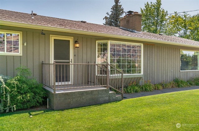 view of exterior entry featuring board and batten siding, roof with shingles, a lawn, and a chimney