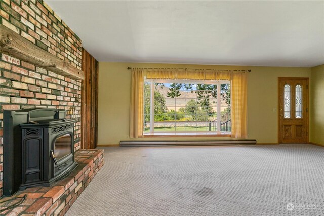 unfurnished living room featuring carpet, a wood stove, baseboards, and a baseboard radiator