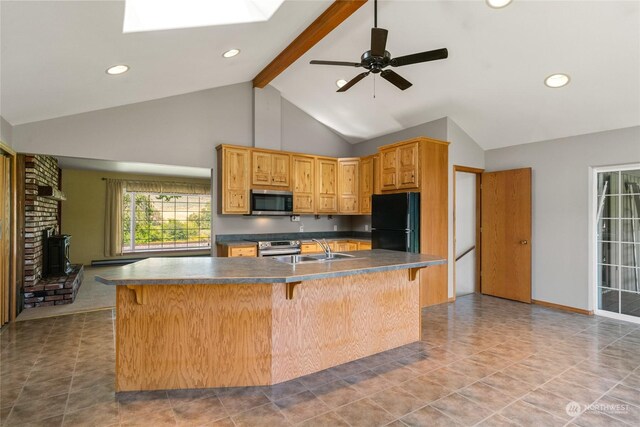 kitchen with a sink, beam ceiling, freestanding refrigerator, stainless steel microwave, and dark countertops