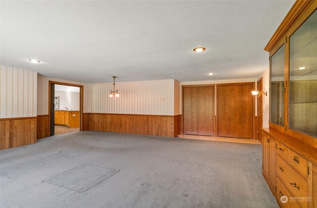 unfurnished room featuring a textured ceiling, wainscoting, light carpet, and wallpapered walls