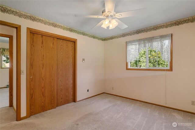 unfurnished bedroom featuring a ceiling fan, baseboards, a closet, and light colored carpet