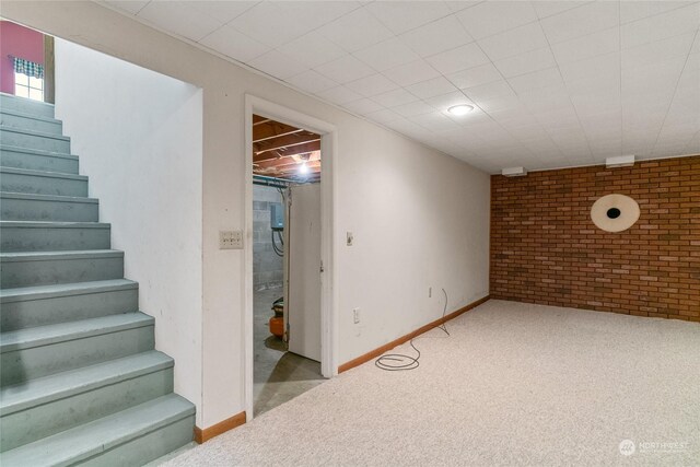 finished basement with brick wall, stairs, baseboards, and light colored carpet