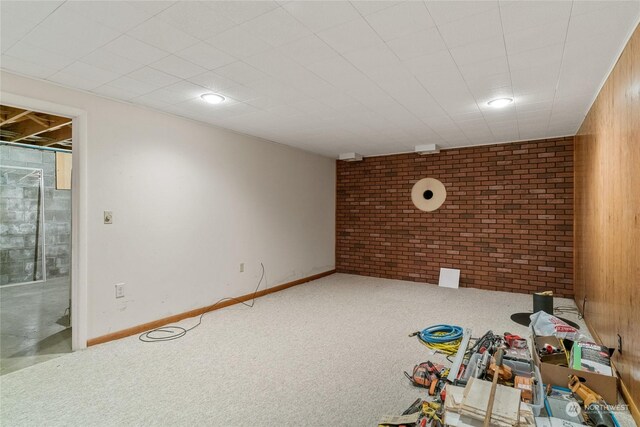 finished basement with brick wall, carpet, and baseboards