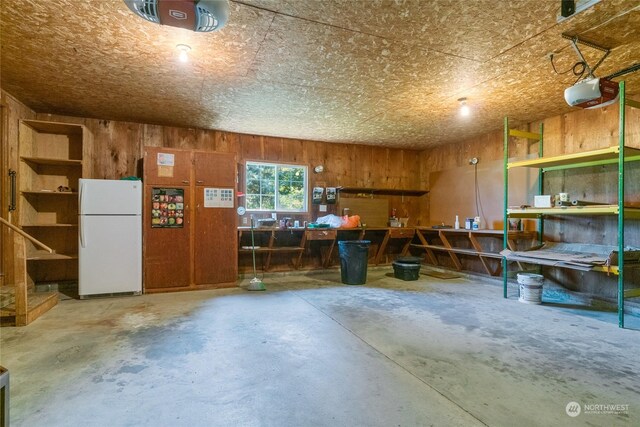 garage with wood walls, a garage door opener, a workshop area, and freestanding refrigerator