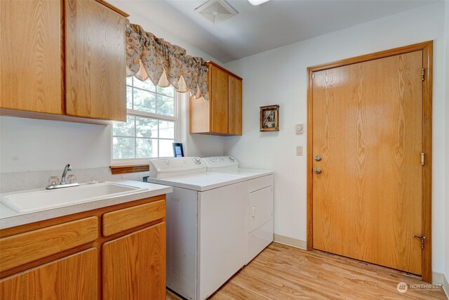 laundry area with light hardwood / wood-style floors, sink, independent washer and dryer, and cabinets