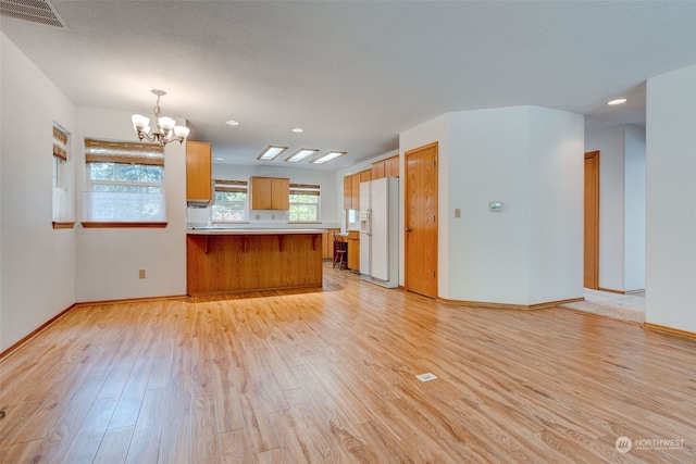 kitchen with light wood-type flooring, pendant lighting, white refrigerator with ice dispenser, kitchen peninsula, and a notable chandelier