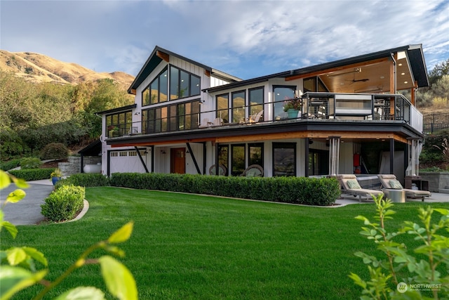 rear view of house with a lawn, a mountain view, ceiling fan, a patio, and a balcony