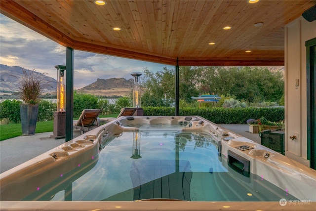 pool at dusk featuring a mountain view, a hot tub, and a patio