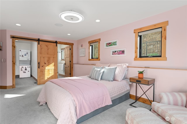 bedroom with a barn door, light colored carpet, and connected bathroom