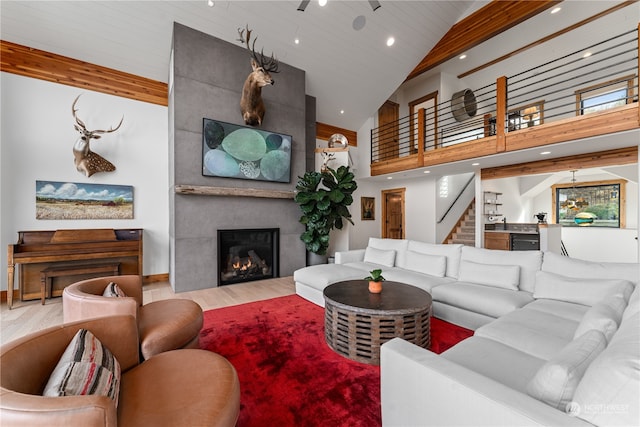 living room featuring high vaulted ceiling, a large fireplace, ceiling fan, hardwood / wood-style flooring, and beam ceiling