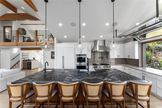 kitchen featuring wall chimney range hood, dark stone countertops, a large island, and beam ceiling