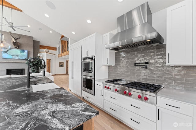 kitchen with wall chimney range hood, ceiling fan, light wood-type flooring, and tasteful backsplash