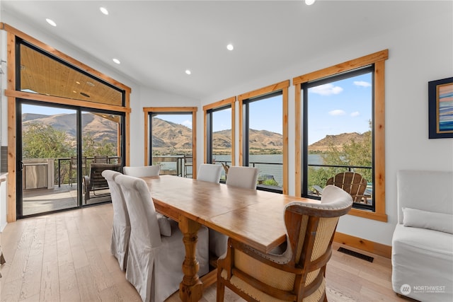 dining room featuring lofted ceiling, a water and mountain view, light hardwood / wood-style floors, and a healthy amount of sunlight