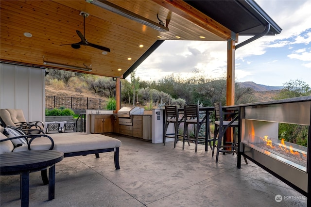 view of patio / terrace featuring a fire pit, a mountain view, an outdoor bar, ceiling fan, and an outdoor kitchen