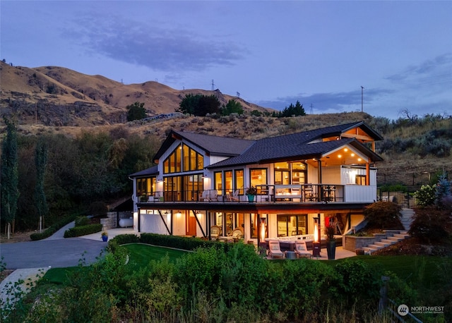 back house at dusk featuring outdoor lounge area, a patio area, a mountain view, and a balcony