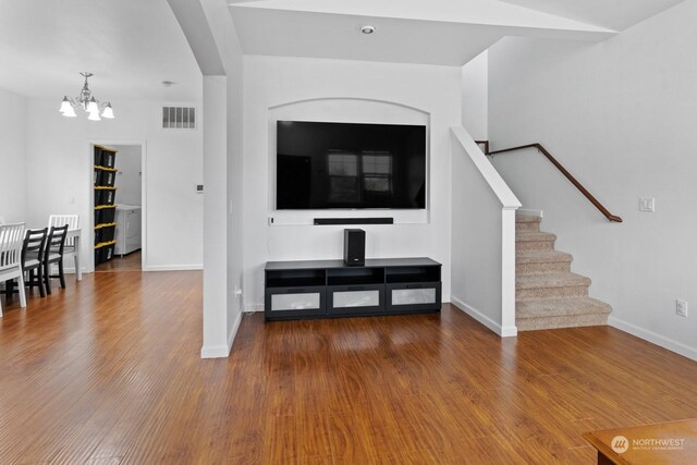 unfurnished living room with washer / clothes dryer, an inviting chandelier, and hardwood / wood-style floors