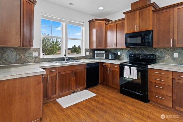 kitchen with tasteful backsplash, sink, black appliances, tile counters, and dark wood-type flooring