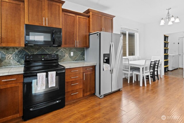 kitchen featuring decorative backsplash, tile counters, a chandelier, hardwood / wood-style floors, and black appliances