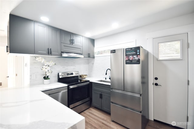 kitchen with gray cabinetry, tasteful backsplash, light hardwood / wood-style floors, stainless steel appliances, and sink