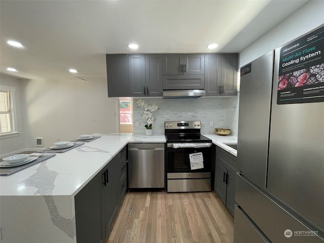 kitchen with light hardwood / wood-style flooring, light stone counters, stainless steel appliances, gray cabinets, and tasteful backsplash