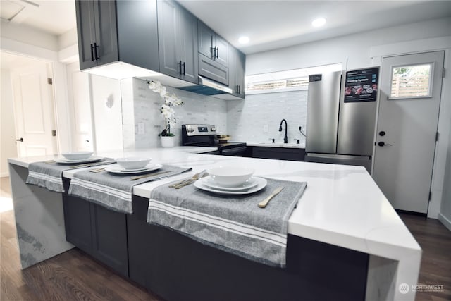 kitchen featuring dark hardwood / wood-style floors, appliances with stainless steel finishes, tasteful backsplash, kitchen peninsula, and sink