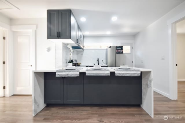 kitchen with gray cabinetry, stainless steel fridge, tasteful backsplash, kitchen peninsula, and hardwood / wood-style flooring