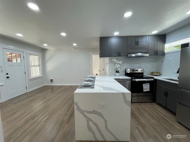 kitchen with light stone countertops, stainless steel appliances, gray cabinets, decorative backsplash, and hardwood / wood-style flooring