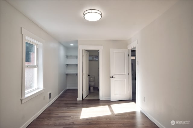 unfurnished bedroom with dark wood-type flooring, a closet, a spacious closet, and ensuite bathroom