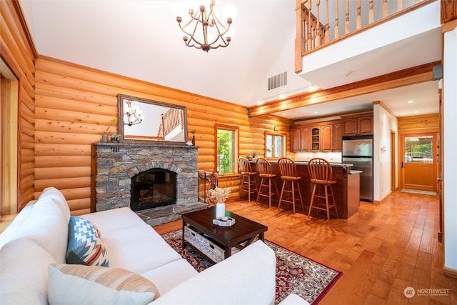 living room with log walls, an inviting chandelier, light hardwood / wood-style floors, a fireplace, and high vaulted ceiling