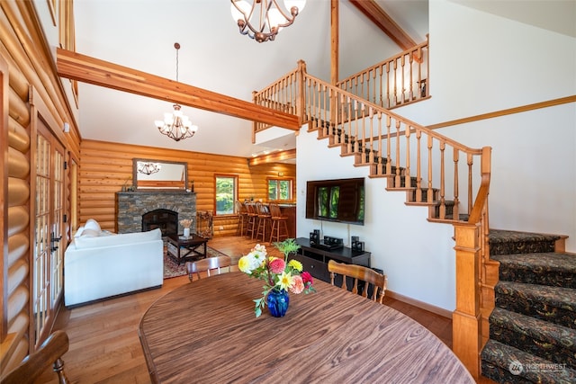 dining room with beamed ceiling, rustic walls, hardwood / wood-style flooring, a stone fireplace, and high vaulted ceiling