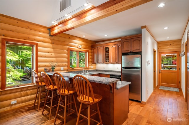 kitchen with light hardwood / wood-style floors, rustic walls, kitchen peninsula, stainless steel refrigerator, and a breakfast bar area