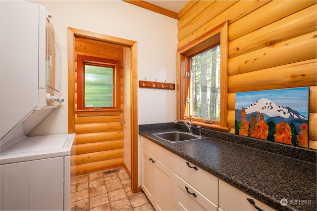 kitchen featuring log walls, white cabinetry, sink, stacked washer and clothes dryer, and ornamental molding