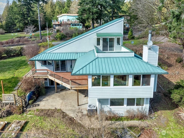 rear view of house with metal roof, stairway, a wooden deck, a standing seam roof, and a chimney