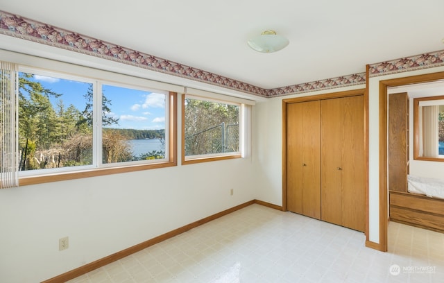 unfurnished bedroom with light floors, a closet, a water view, and baseboards