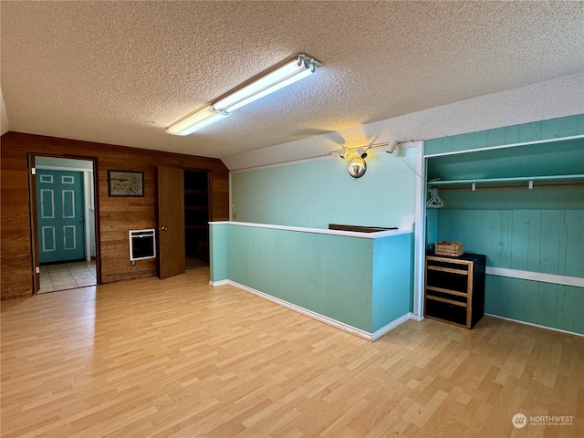 interior space with a textured ceiling, light hardwood / wood-style flooring, and wood walls