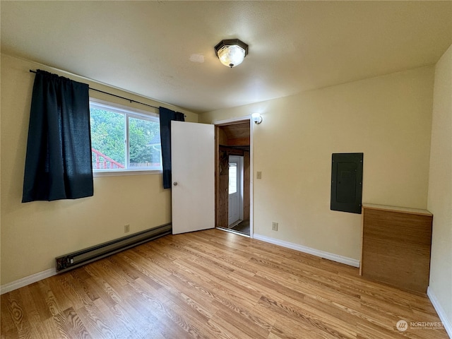 empty room featuring light wood-type flooring, baseboard heating, and electric panel