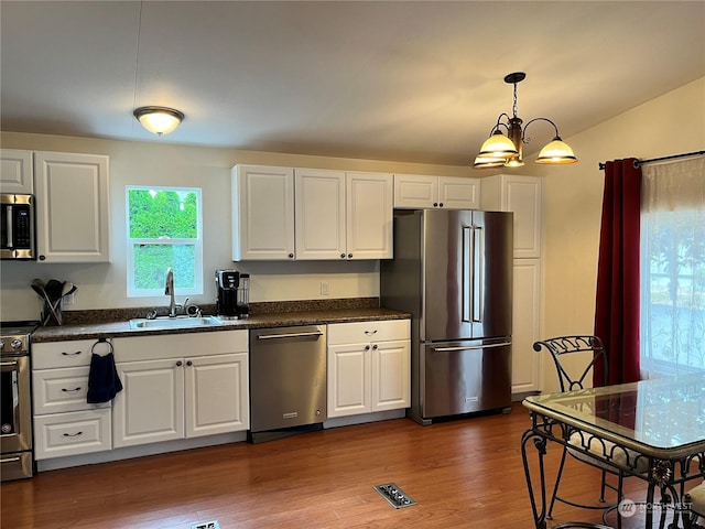 kitchen with sink, dark wood-type flooring, appliances with stainless steel finishes, white cabinetry, and decorative light fixtures