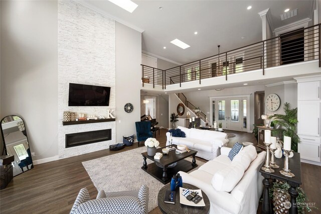 living room featuring a towering ceiling, a stone fireplace, crown molding, and dark hardwood / wood-style flooring