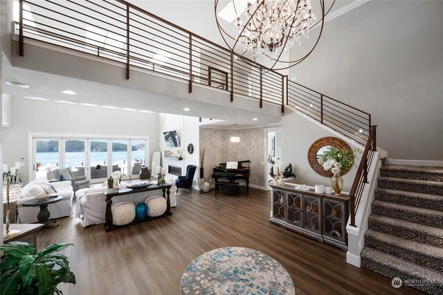 living room with a towering ceiling, dark wood-type flooring, a water view, and a chandelier