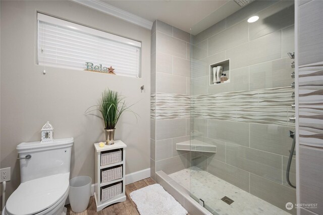 bathroom with wood-type flooring, a tile shower, crown molding, and toilet