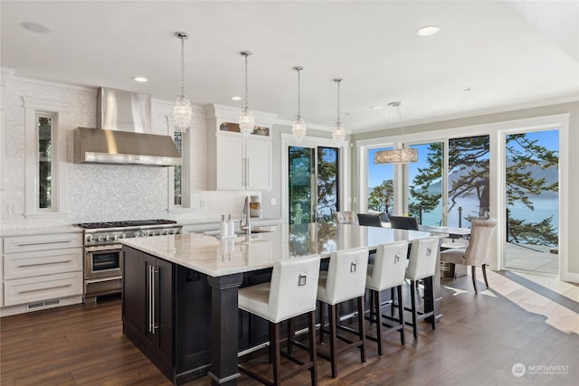 kitchen with wall chimney exhaust hood, white cabinets, an island with sink, and double oven range