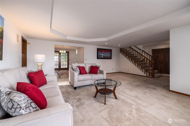 living room featuring baseboards, a raised ceiling, light colored carpet, stairs, and a chandelier