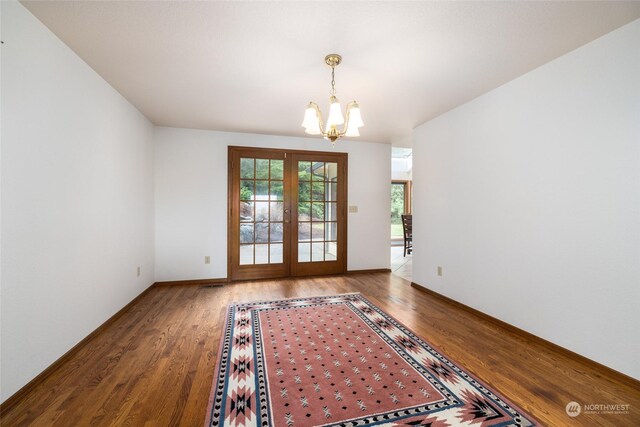 empty room with hardwood / wood-style flooring, an inviting chandelier, and french doors