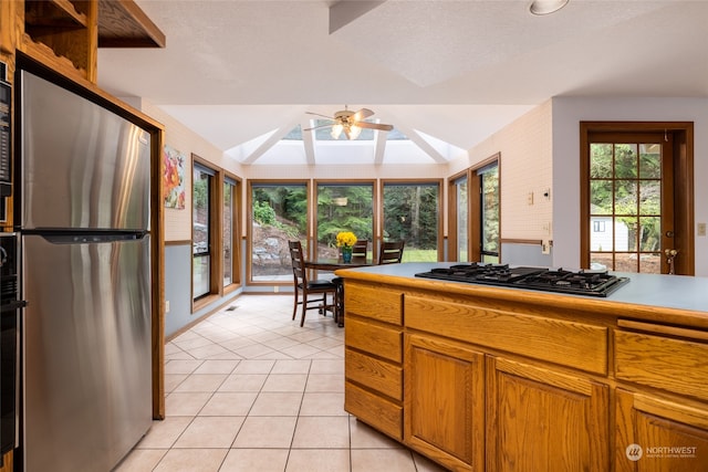 kitchen featuring black gas cooktop, vaulted ceiling with skylight, stainless steel refrigerator, light tile patterned floors, and ceiling fan