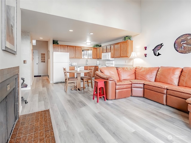 living room with sink, light wood-type flooring, and a tile fireplace