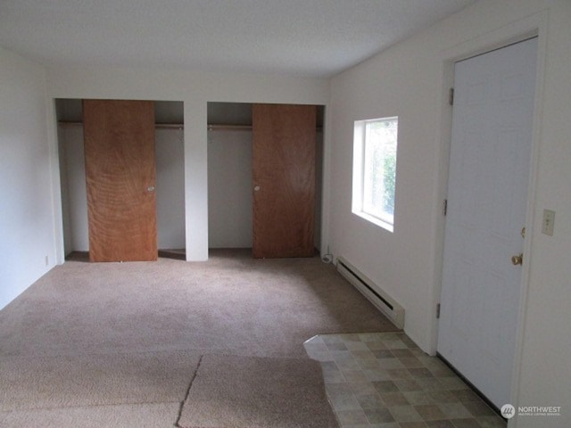 unfurnished bedroom featuring a baseboard heating unit, two closets, and dark colored carpet