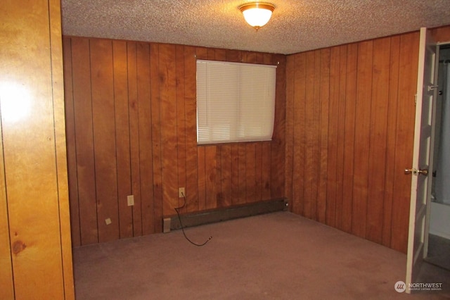 spare room with a textured ceiling, a baseboard radiator, carpet, and wood walls