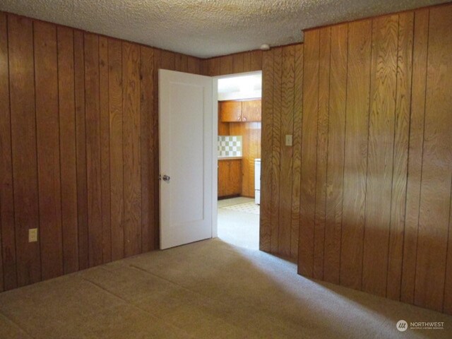 spare room with a textured ceiling, wooden walls, and light carpet