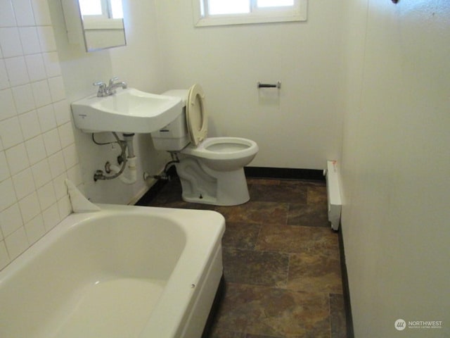 full bath with baseboards, a sink, toilet, stone finish floor, and a washtub